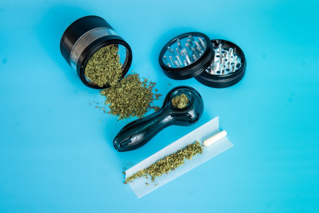 cannabis accessories on blue surface including grinder, bowl and cannabis joint